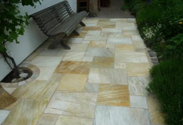 Außenbereich gefliest mit Natrustein mit Hausbank vor dem Garten