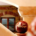 Dekorative Kugel auf einem Sockel vor einem Fenster mit gemauertem Rundbogen in warmem Licht.