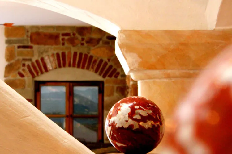 Dekorative Kugel auf einem Sockel vor einem Fenster mit gemauertem Rundbogen in warmem Licht.