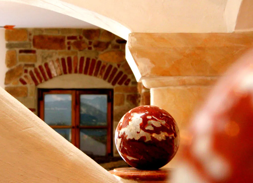 Dekorative Kugel auf einem Sockel vor einem Fenster mit gemauertem Rundbogen in warmem Licht.