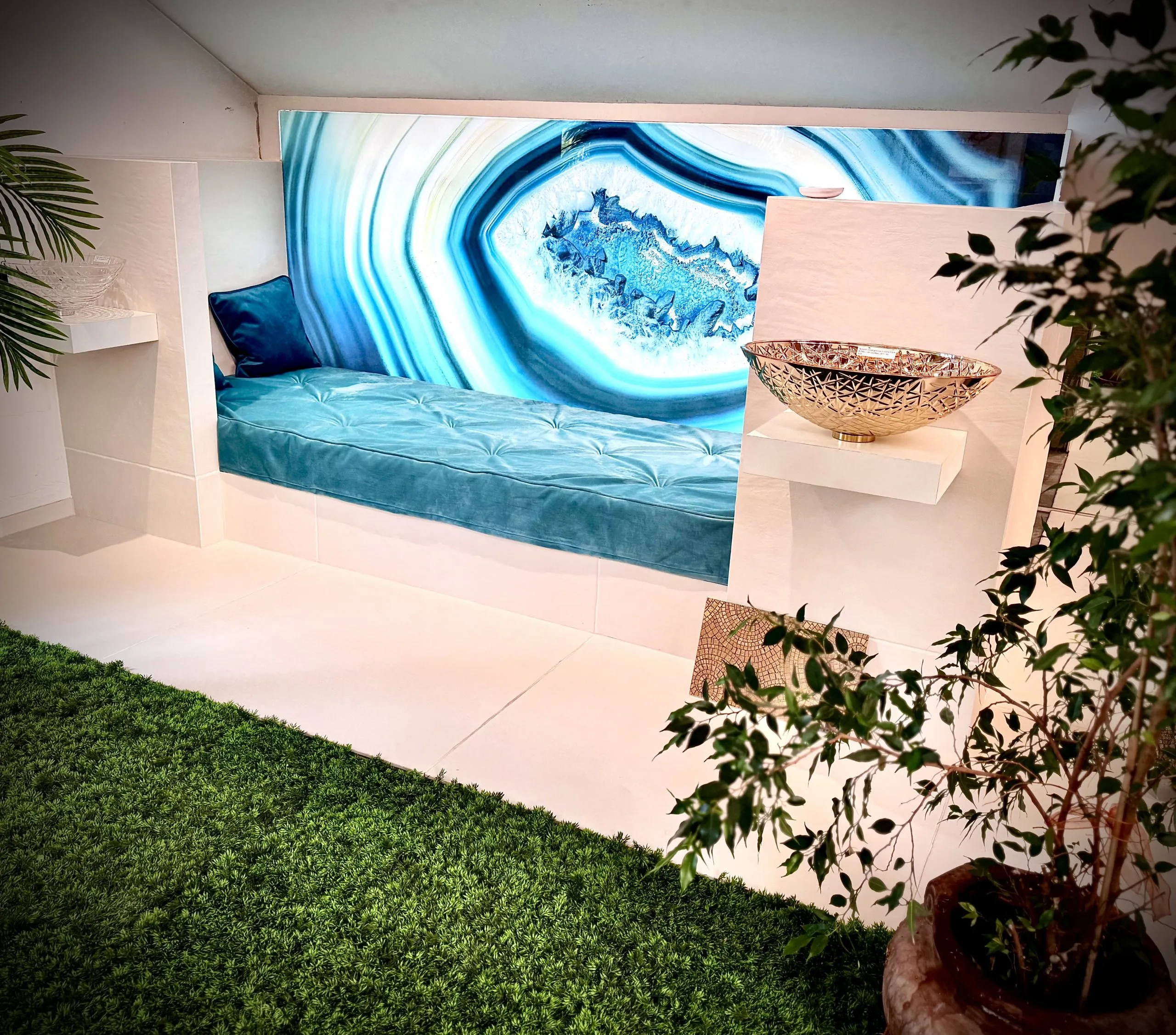 Liege mit Hinterleuchteter Glasplatte mit blausteinoptik. Sehr schön dekoriert mit Pflanzen und Palmen. rechts auf einem Sockel steht ein silberner Waschtisch.