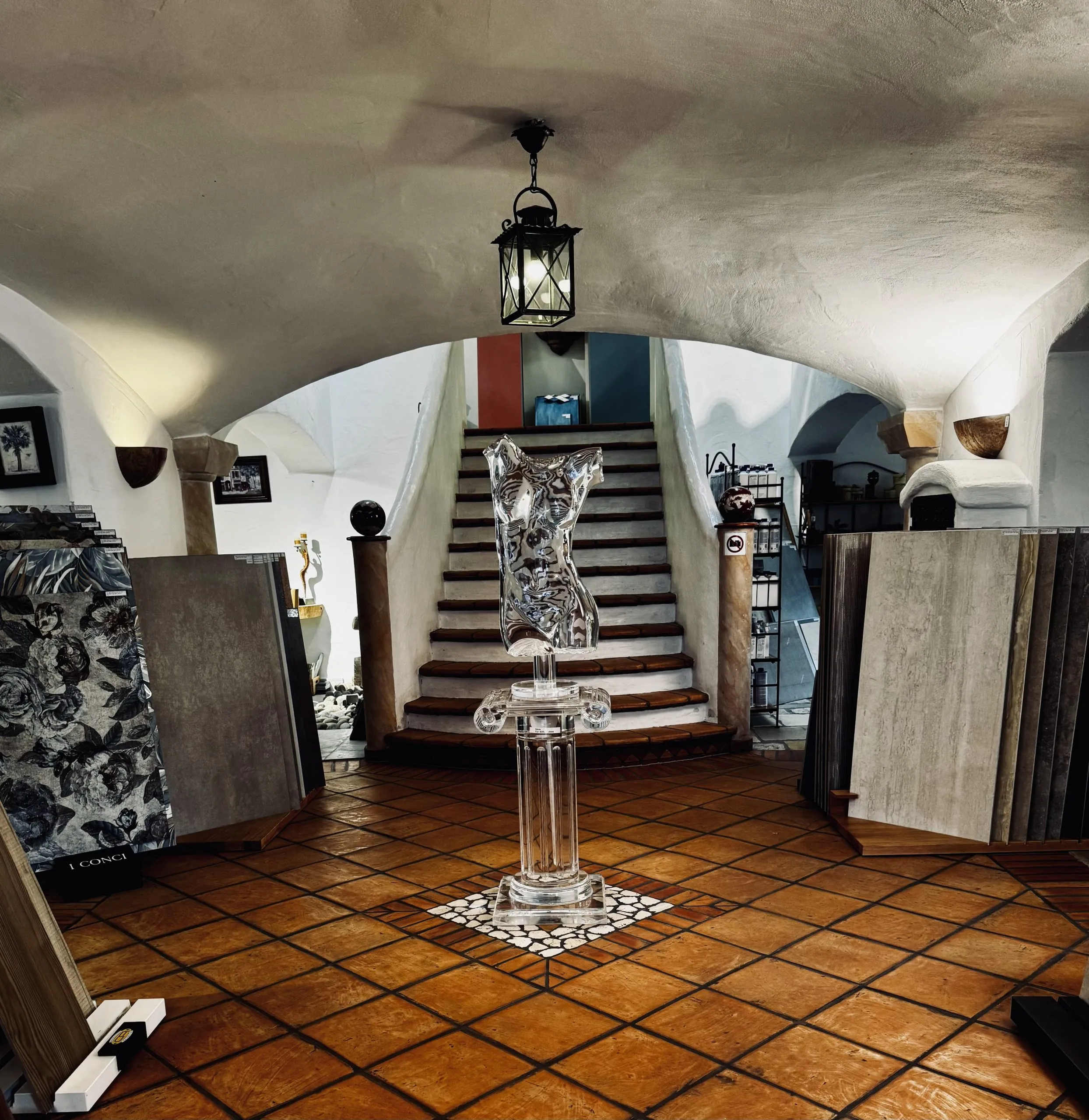 Eingangsbereich EG Eingangsbereich der Ausstellung im Erdgeschoss mit Cotto Boden . Zu sehen sind einige Fliesenmuster und eine Acrylskulptur in Form eines Oberkörpers.