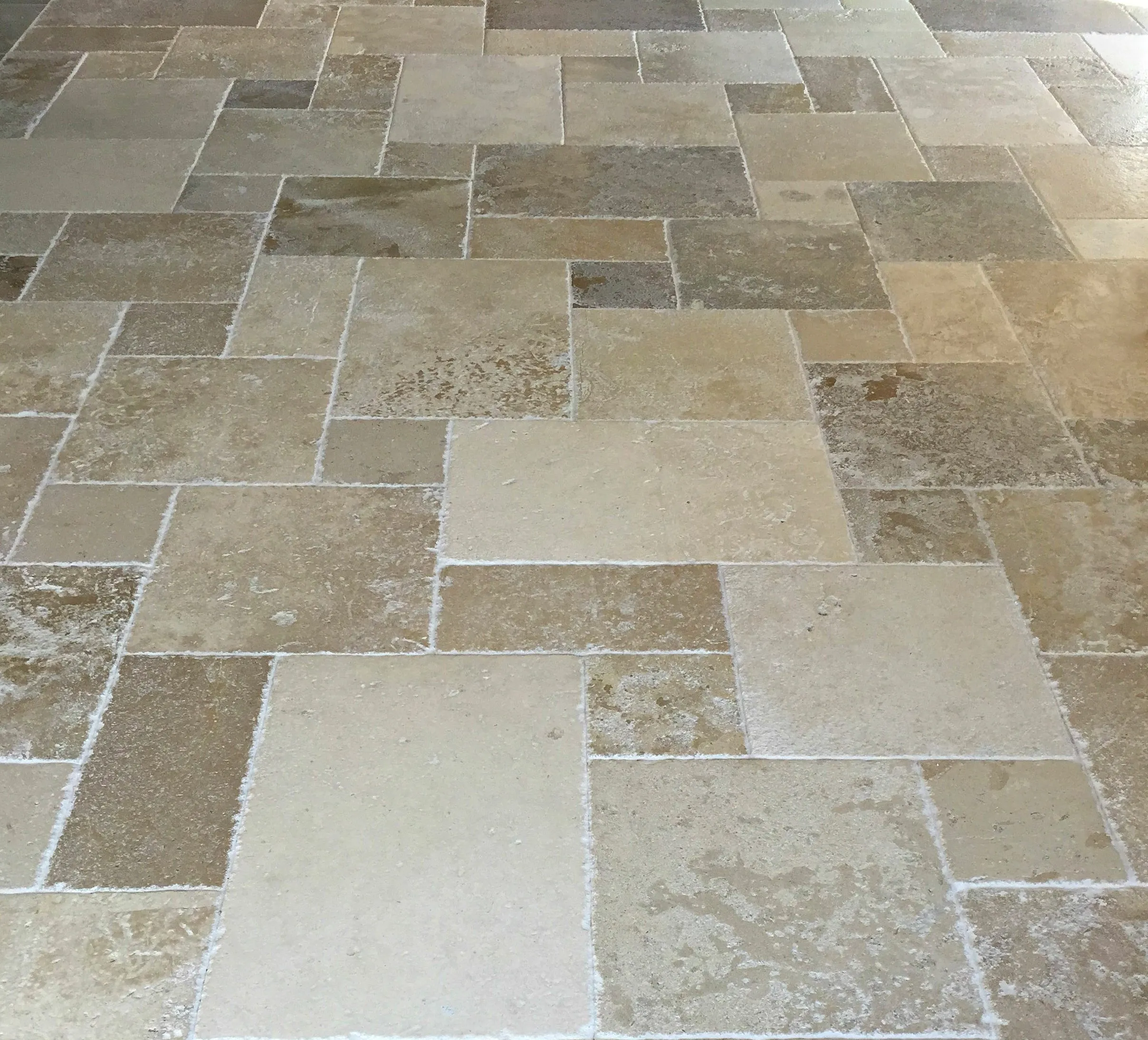 Travertin Der abgebildete Naturstein ist ein Travertin Typisch dafür sind: beige- bis hellbraune Farbpalette, die porige, leicht unregelmäßige Oberfläche, und die unterschiedlichen Schattierungen innerhalb der einzelnen Platten. Das Verlegemuster ist ein sogenanntes römischer Verband (Opus Romano), der häufig bei Travertin verwendet wird, um ein mediterranes, natürliches Erscheinungsbild zu erzeugen.